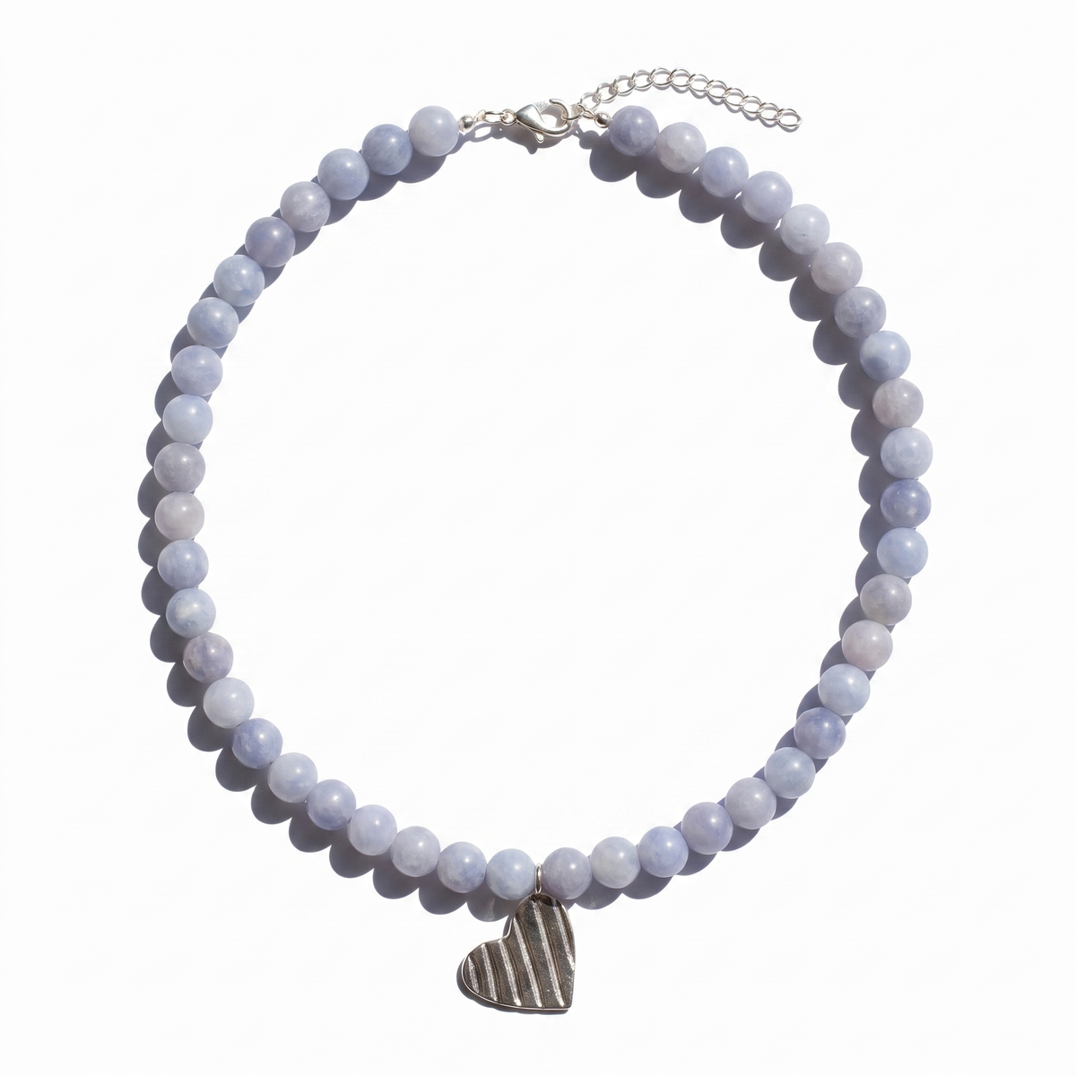 A beaded necklace featuring pale lavender and light blue-gray round beads, with a textured silver heart pendant and silver clasp, displayed on a clean white background.