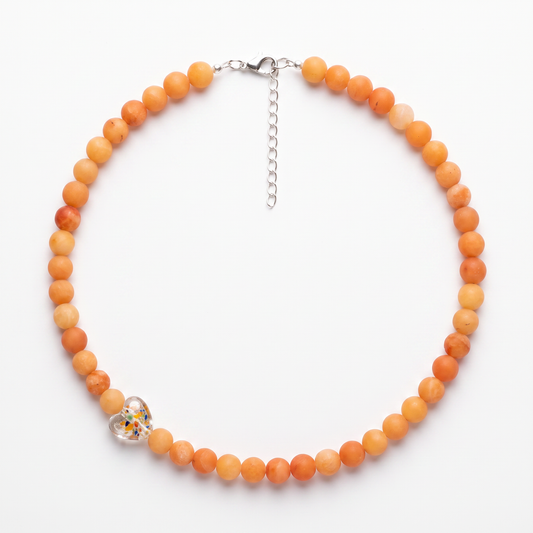 A beaded necklace made of round orange beads, with a small heart charm containing colorful inlay details, displayed on a clean white background.