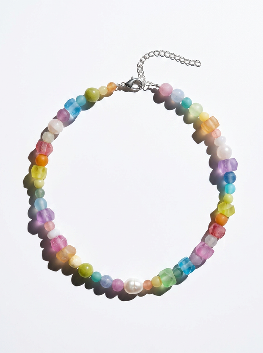 A beaded necklace with small, translucent, multi-colored round beads in pastel rainbow shades, arranged in a circle on a white background. It features a silver-tone lobster clasp and a silver-tone extender chain.