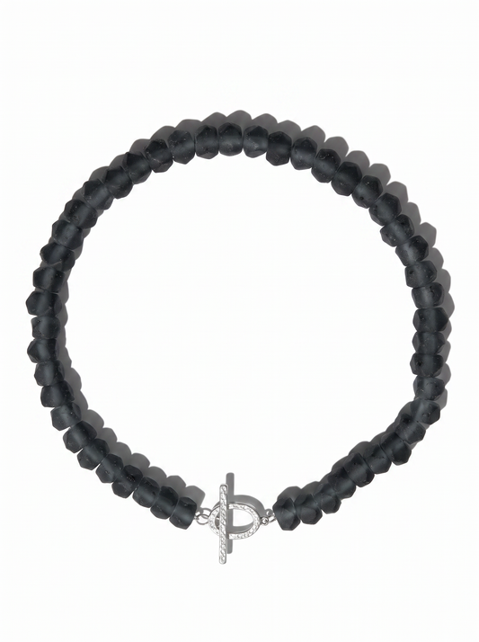A beaded stretch bracelet made of faceted dark gray beads, featuring a silver-toned toggle clasp with a textured design, shown on a plain white background.