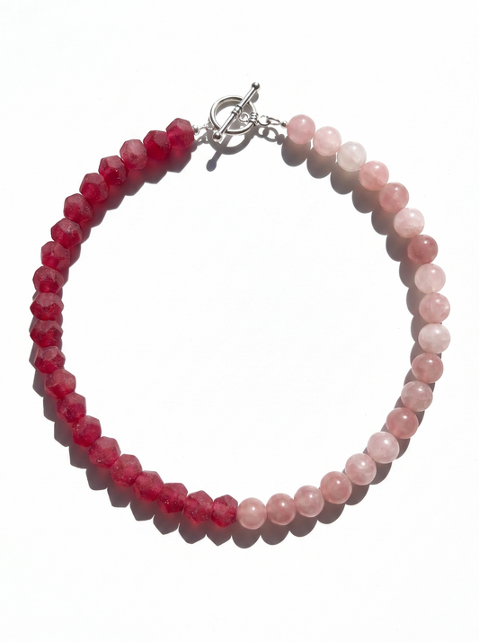 A beaded necklace made of faceted dark red beads on one side and smooth light pink beads on the other, with a silver toggle clasp, shown on a white background.