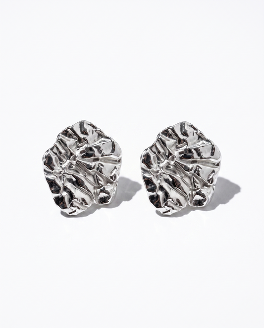 A pair of silver-toned, organic-shaped stud earrings with a highly textured, crumpled surface, displayed on a clean white background with soft shadows.